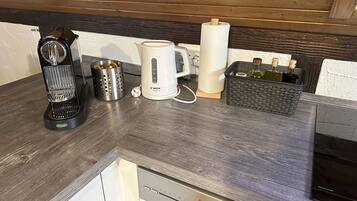 A kitchen counter with a coffee maker, a kettle, a paper towel holder, and a basket with bottles.