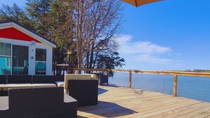 Eine Holzterrasse mit Gartenmöbeln, einem überdachten Bereich und Blick auf das Wasser.