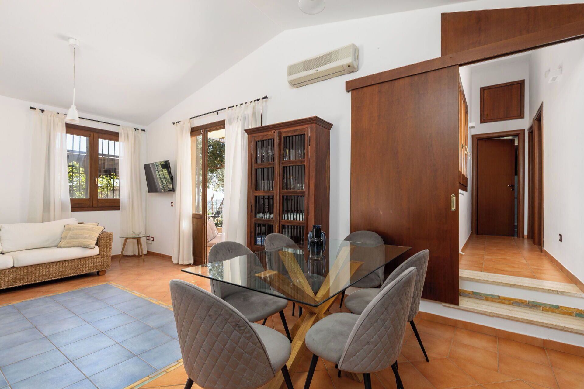 Amplia sala de estar con mesa de vidrio para comedor, asientos cómodos, televisor y un mueble de madera grande.