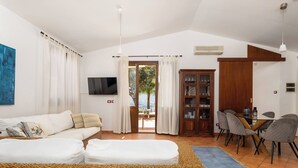 A living room with a sofa, a television, a dining area with chairs, and a bookshelf. - Villa Petra–Villa with pool and tennis court near Scopello, Sicily (Castellammare Del Golfo)