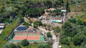 An aerial view of a property with a tennis court, a swimming pool, solar panels, and a stone wall. - Villa Petra–Villa with pool and tennis court near Scopello, Sicily (Castellammare Del Golfo)