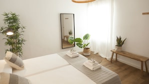 Ein ordentlich eingerichtetes Schlafzimmer mit Bett, Zimmerpflanzen, einem Spiegel und einer Pendelleuchte.