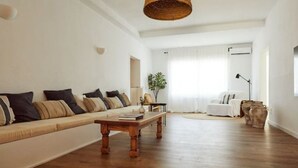 Ein geräumiges Wohnzimmer mit einer langen Couch, einem Holztisch und einer gewebten Pendelleuchte.