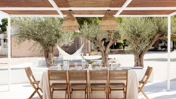 Ein Essbereich im Freien mit einer weißen Pergola, Korbstühlen und einem Tisch für vier Personen.