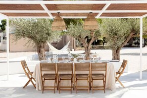 Ein Essbereich im Freien mit einer weißen Pergola, Korbstühlen und einem Tisch für vier Personen.
