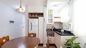 Une cuisine compacte avec des meubles blancs, un four encastré et une table à manger avec des chaises.