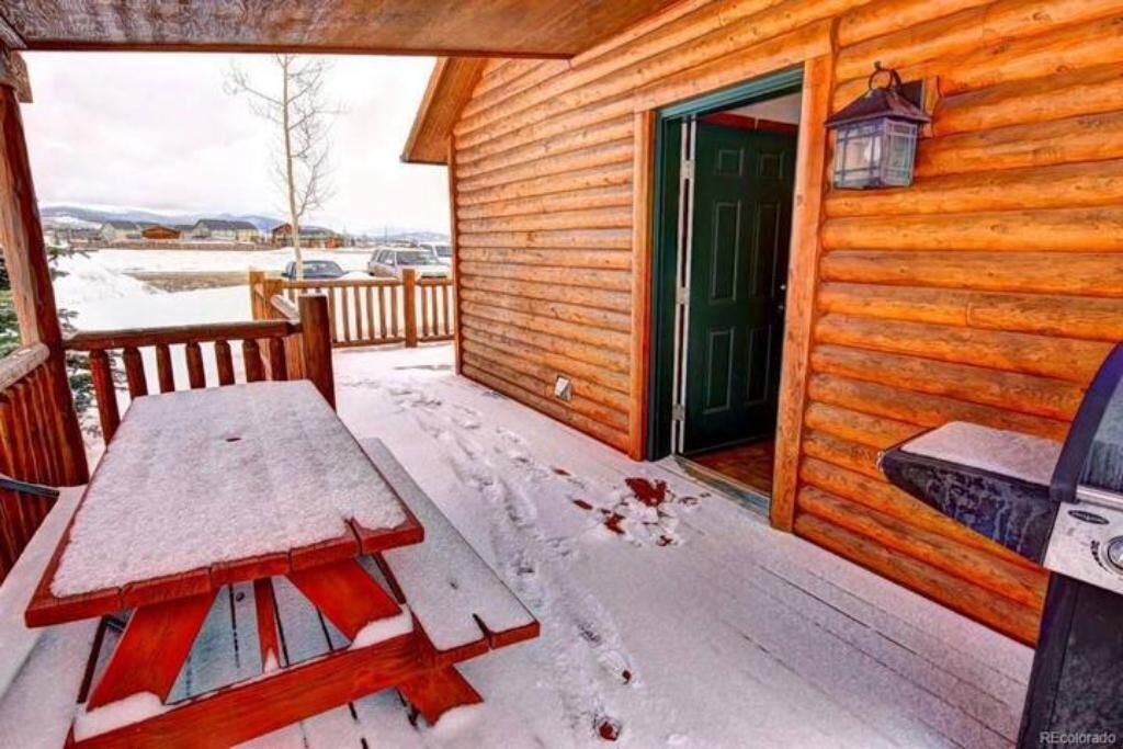 A wooden cabin with a snow-covered deck, a picnic table, and a grill.