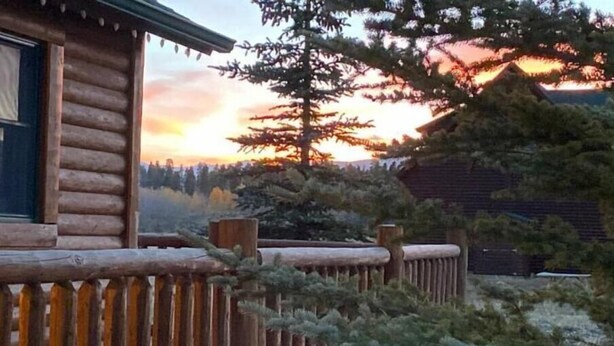 A log cabin with a wooden deck and a view of a forested landscape during sunset. - Cozy Two Bedroom Cabin Mountain Getaway! (Fairplay)