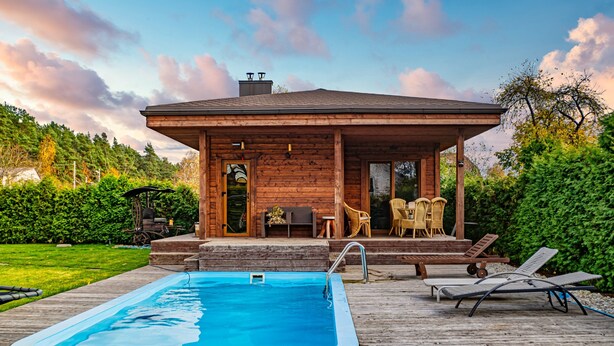 Ein Holzhaus mit Pool, Gartenmöbeln und einer überdachten Terrasse.