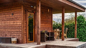 Eine Holzhütte mit Veranda, Sitzgelegenheiten im Freien und Blick auf viel Grün.