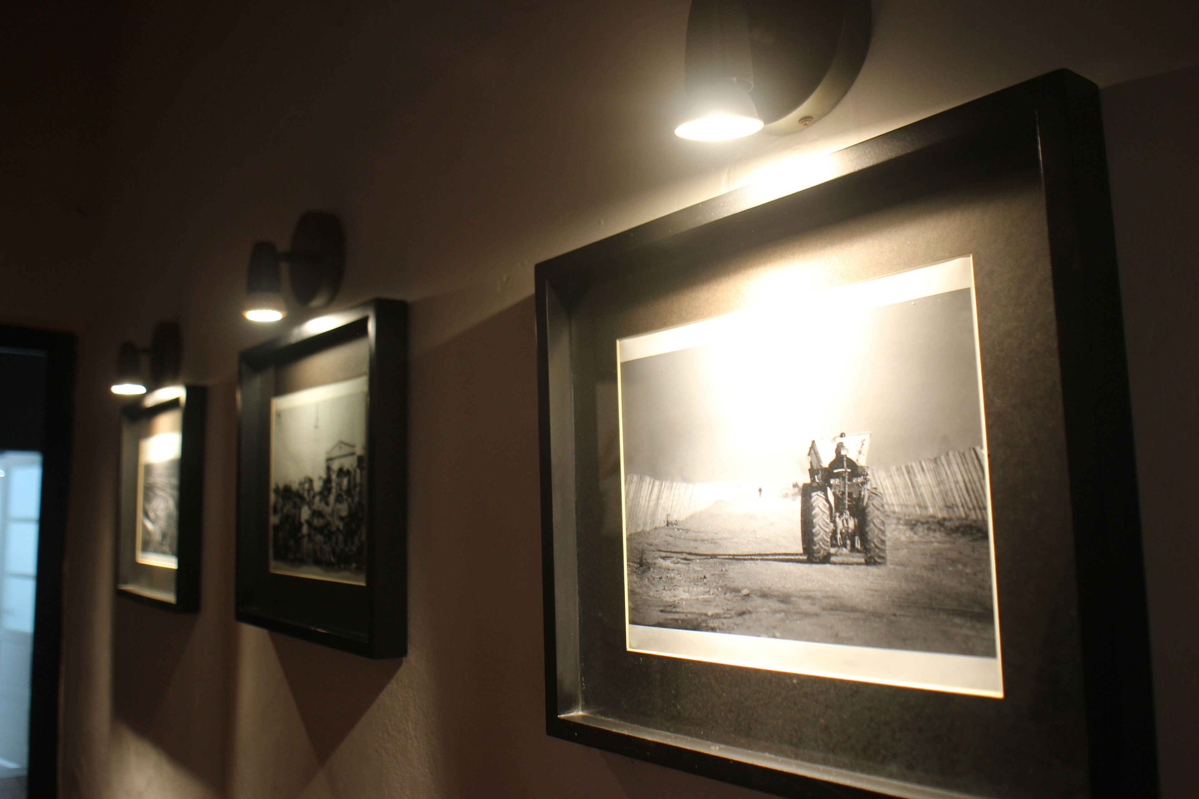 Ein Flur mit gerahmten Fotos an der Wand, jedes beleuchtet von einem Spot.
