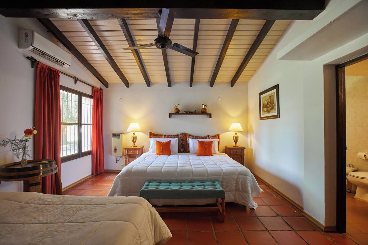 A bedroom with a bed, a bench, a ceiling fan, and a window with curtains.