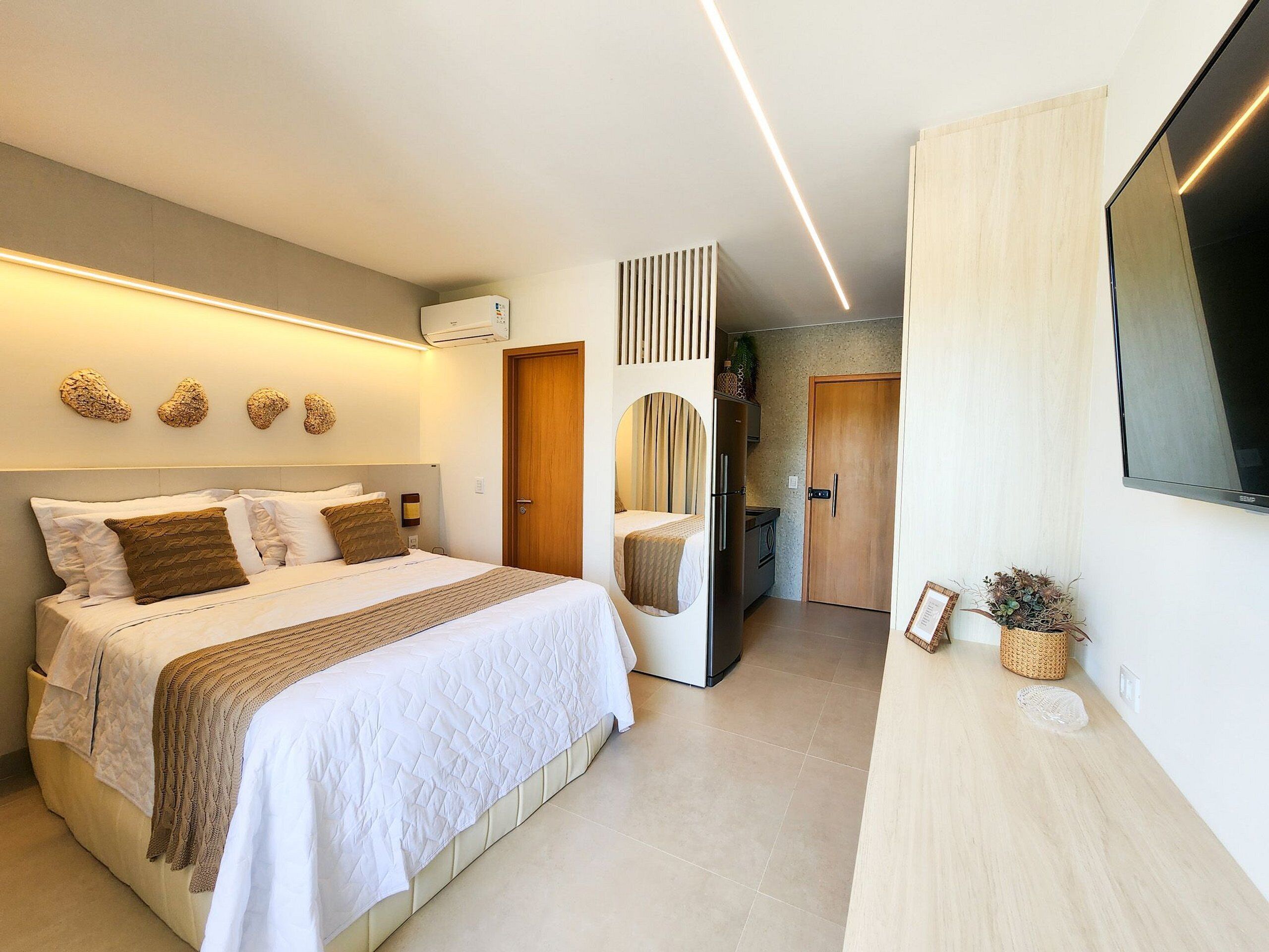 A modern hotel room with a bed, a flat-screen TV, a kitchenette, and a bathroom.