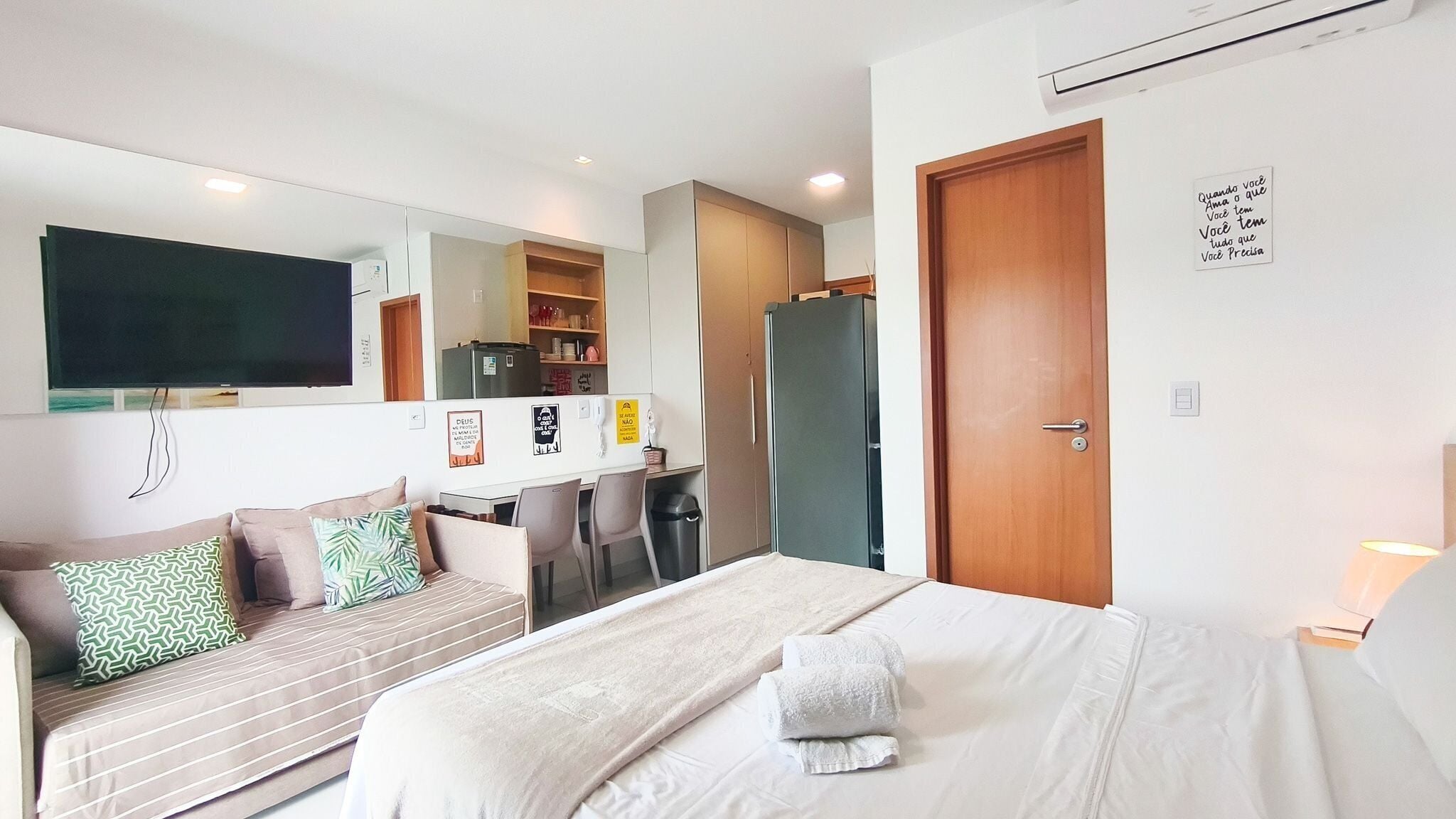 A hotel room with a bed, a sofa, a desk, a TV, and a door.