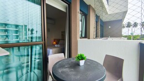 A balcony with a table and chairs, a small potted plant, and a view of a building with a geometric facade. - Makia Beach Experience (Ipojuca)