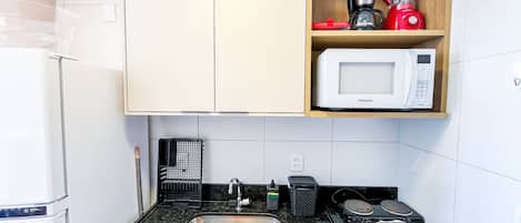 A compact kitchen with a sink, a microwave, and a coffee maker on a shelf.