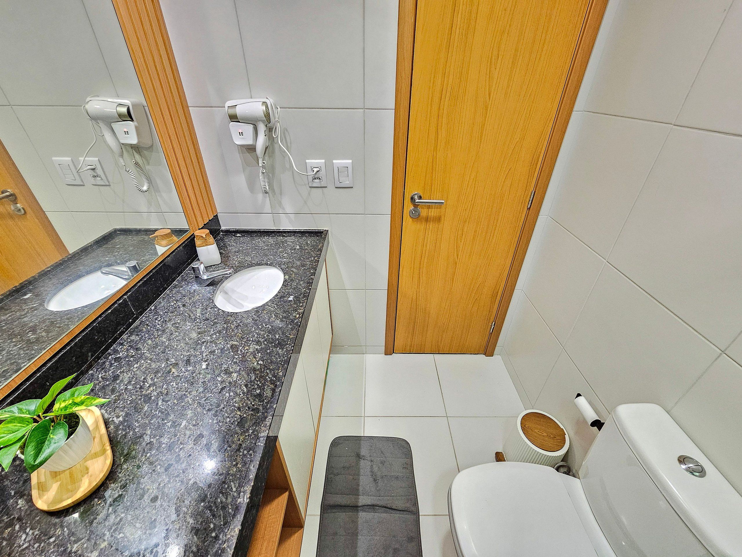 A bathroom with a black marble sink, a mirror, a wooden door, and a toilet.