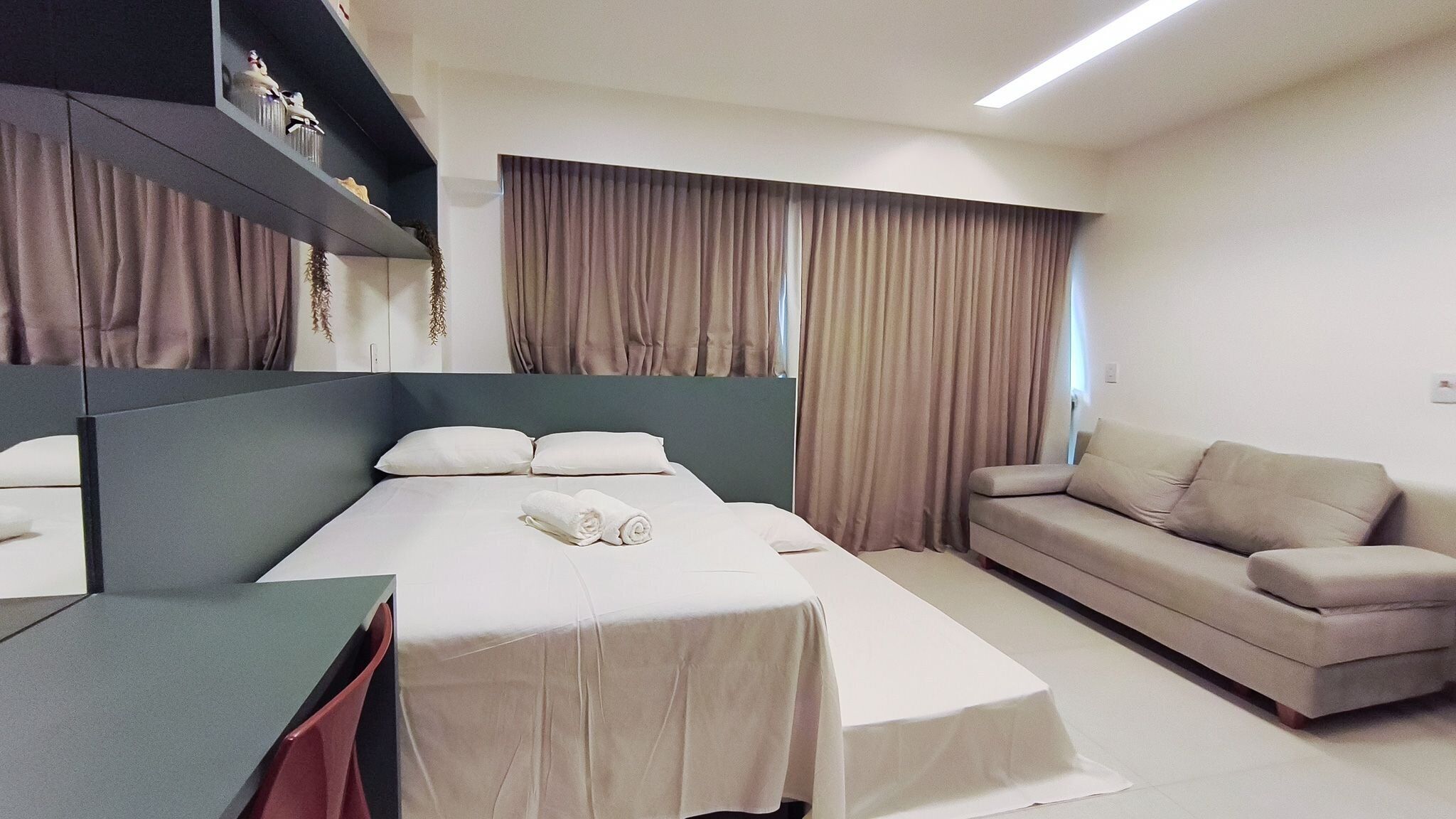 A hotel room with a bed, a sofa, a desk, and a mirror.