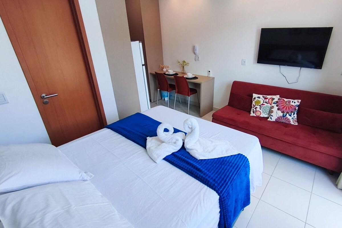 A hotel room with two beds, a red sofa, a TV mounted on the wall, and a small desk with chairs.