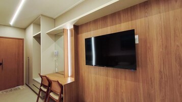 Una habitación con una televisión de pantalla plana montada en una pared de madera, una mesa de comedor de madera con sillas, y una puerta.