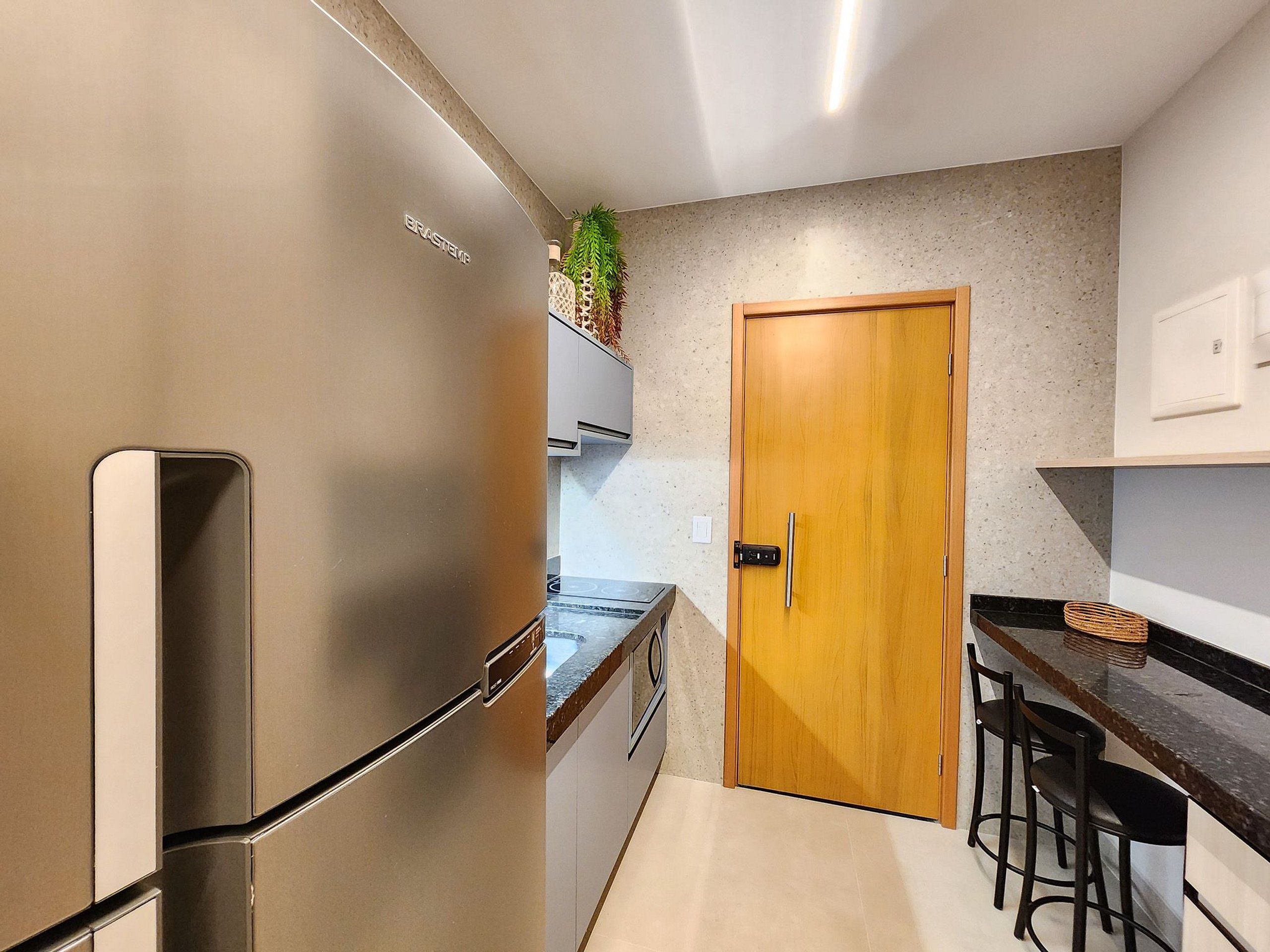 A kitchen with a stainless steel refrigerator, wooden door, and bar stools.