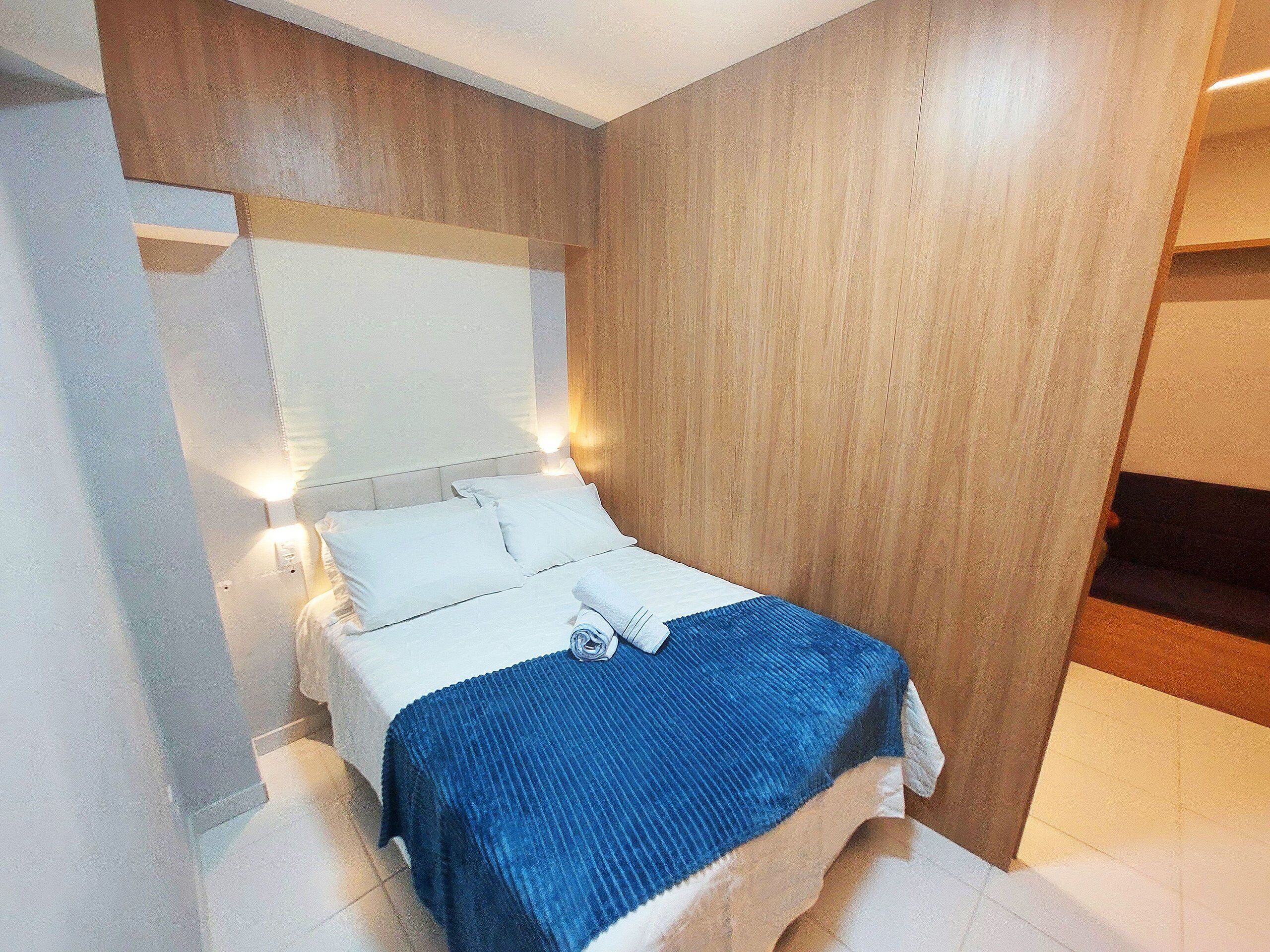A hotel room with a bed, pillows, a blue blanket, and a wooden headboard.