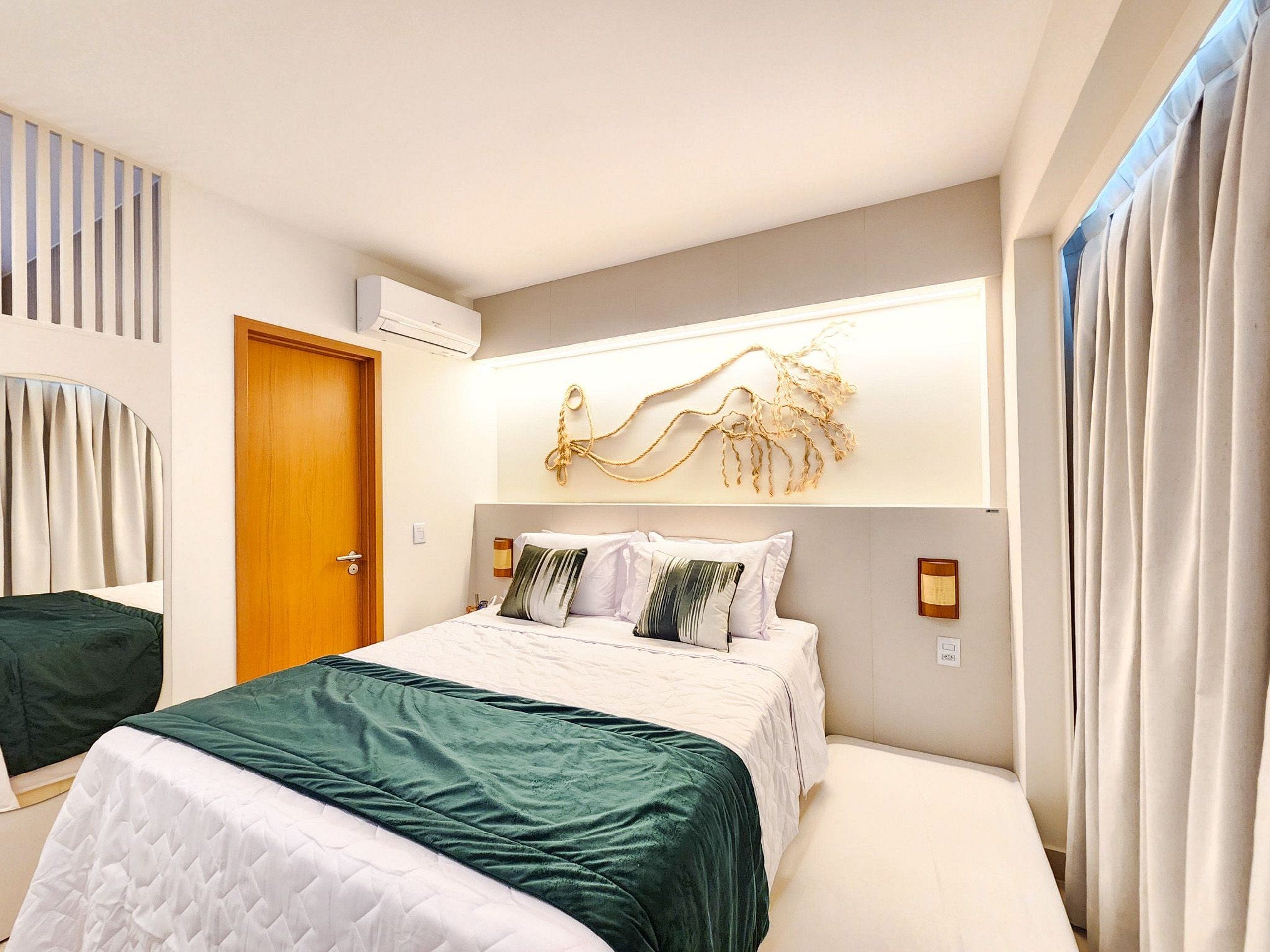 A modern hotel room with a bed, a wooden door, a wall-mounted air conditioner, and a decorative wall piece.
