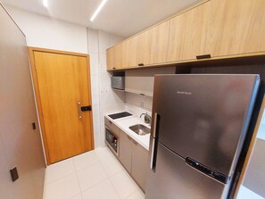 Une cuisine compacte dotée d’un réfrigérateur en acier inoxydable, d’un four encastré et de meubles de rangement en bois.
