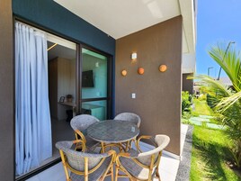 Uma varanda com móveis de vime, uma porta de vidro e um pequeno jardim.