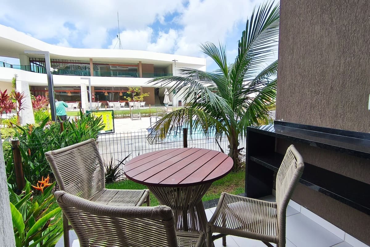 A patio area with wicker chairs and a round table, a pool, and a modern building with balconies.