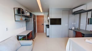 A modern hotel room with a kitchenette, a TV, a desk, and a bed.