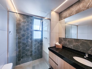 Un baño moderno con cabina de ducha de vidrio, un espejo grande y una encimera negra.