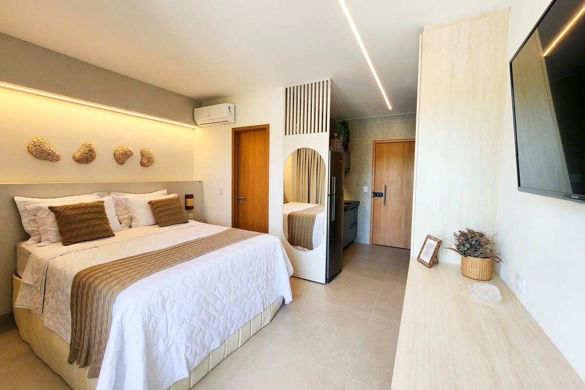 A modern hotel room with a bed, a flat-screen TV, a kitchenette, and a bathroom.