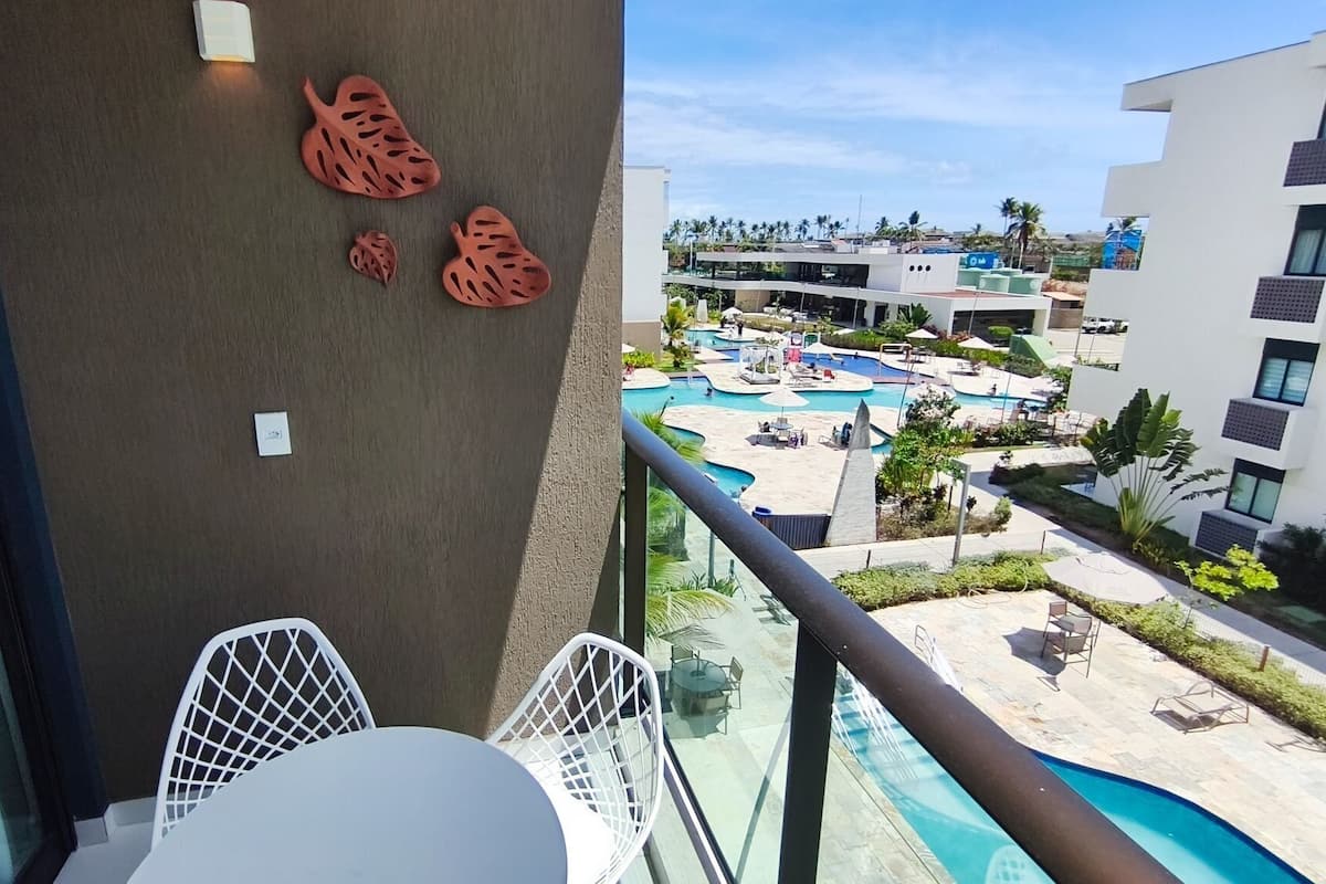 A balcony with a view of a pool area, a white chair, and a table.