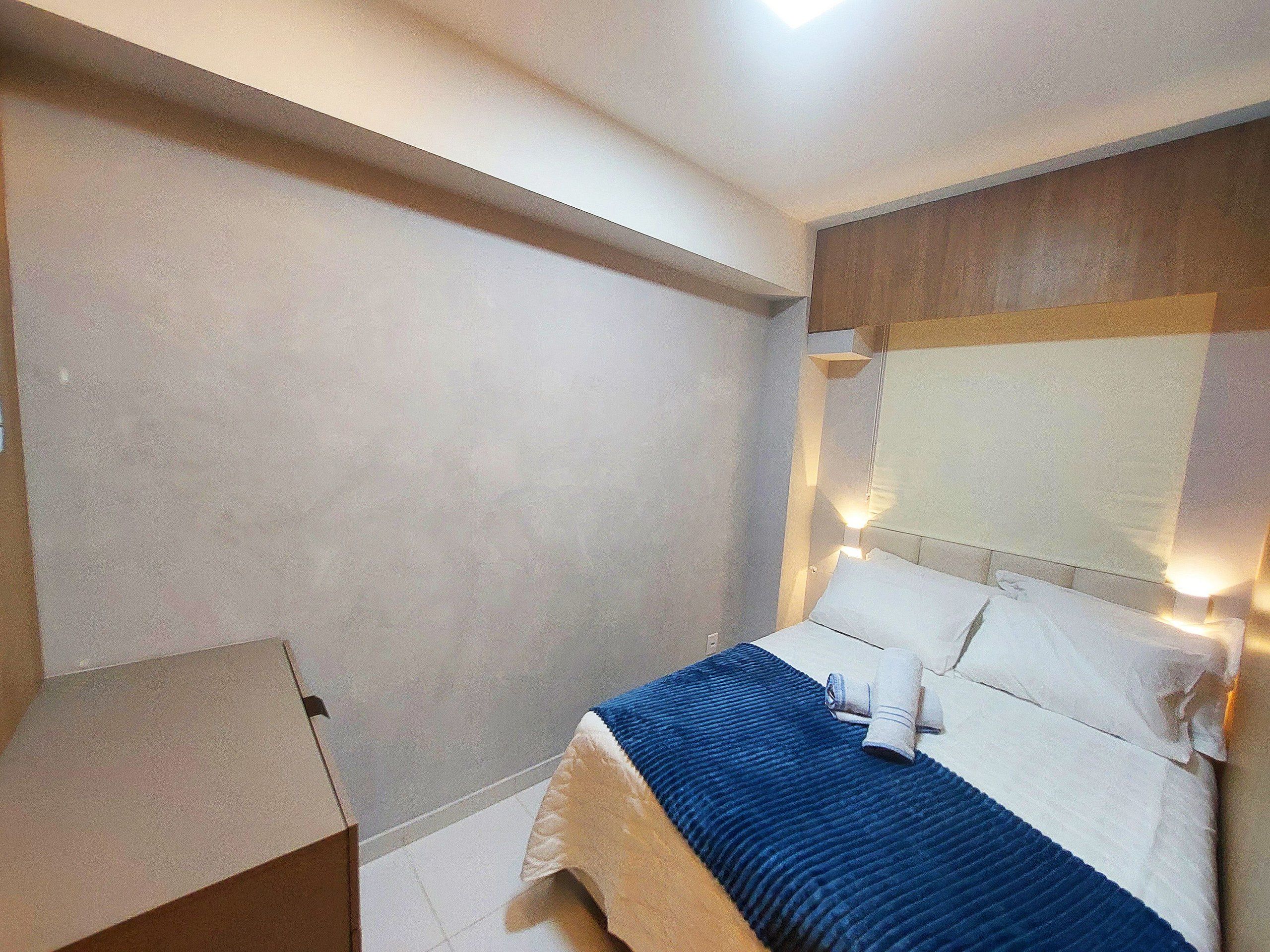 Una habitación de hotel con cama, mesita de noche y cabecera con luces.