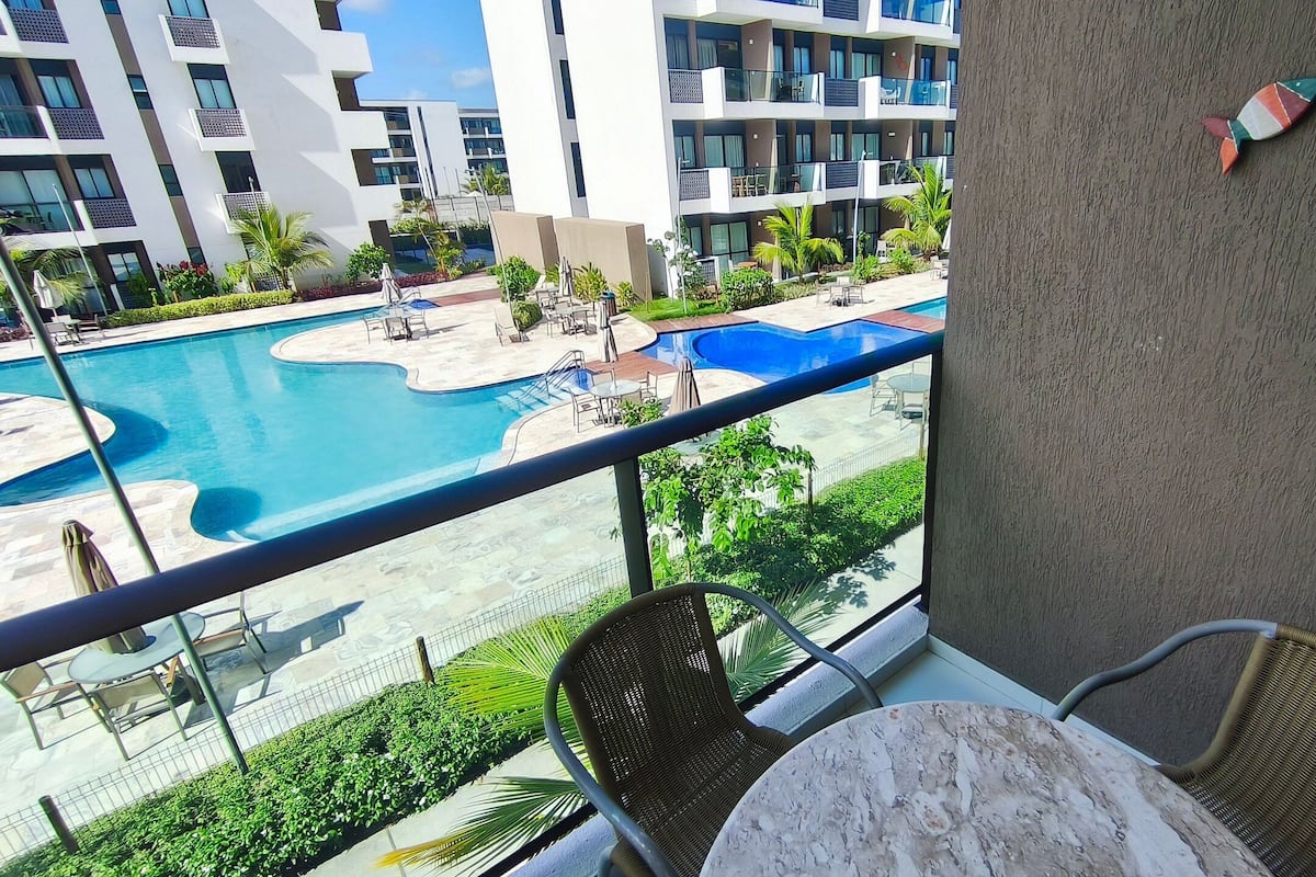 A balcony with a view of a swimming pool, outdoor furniture, and a building with balconies.