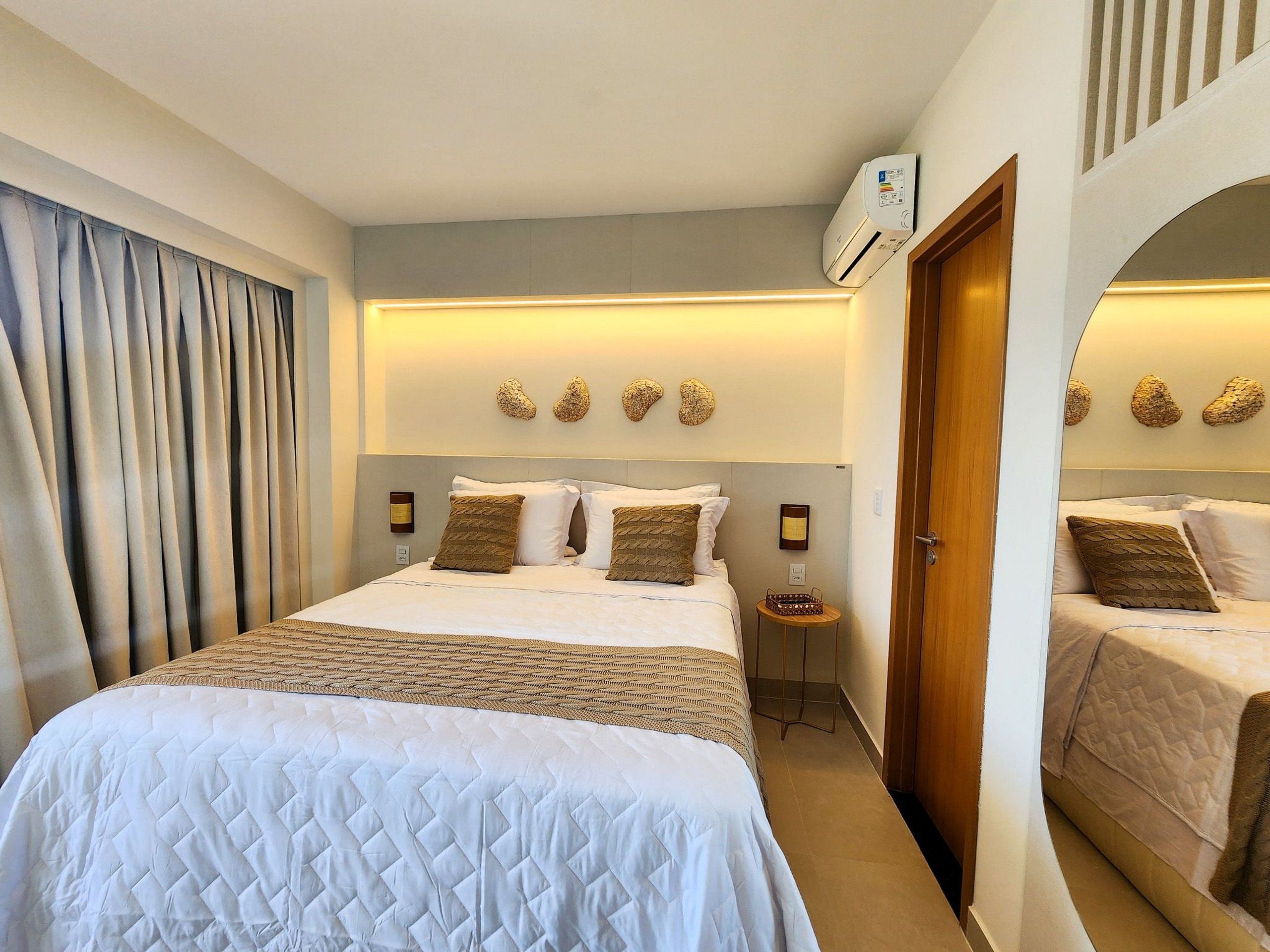 A hotel room with a large bed, a smaller bed, a nightstand, an air conditioning unit, and decorative wall art.