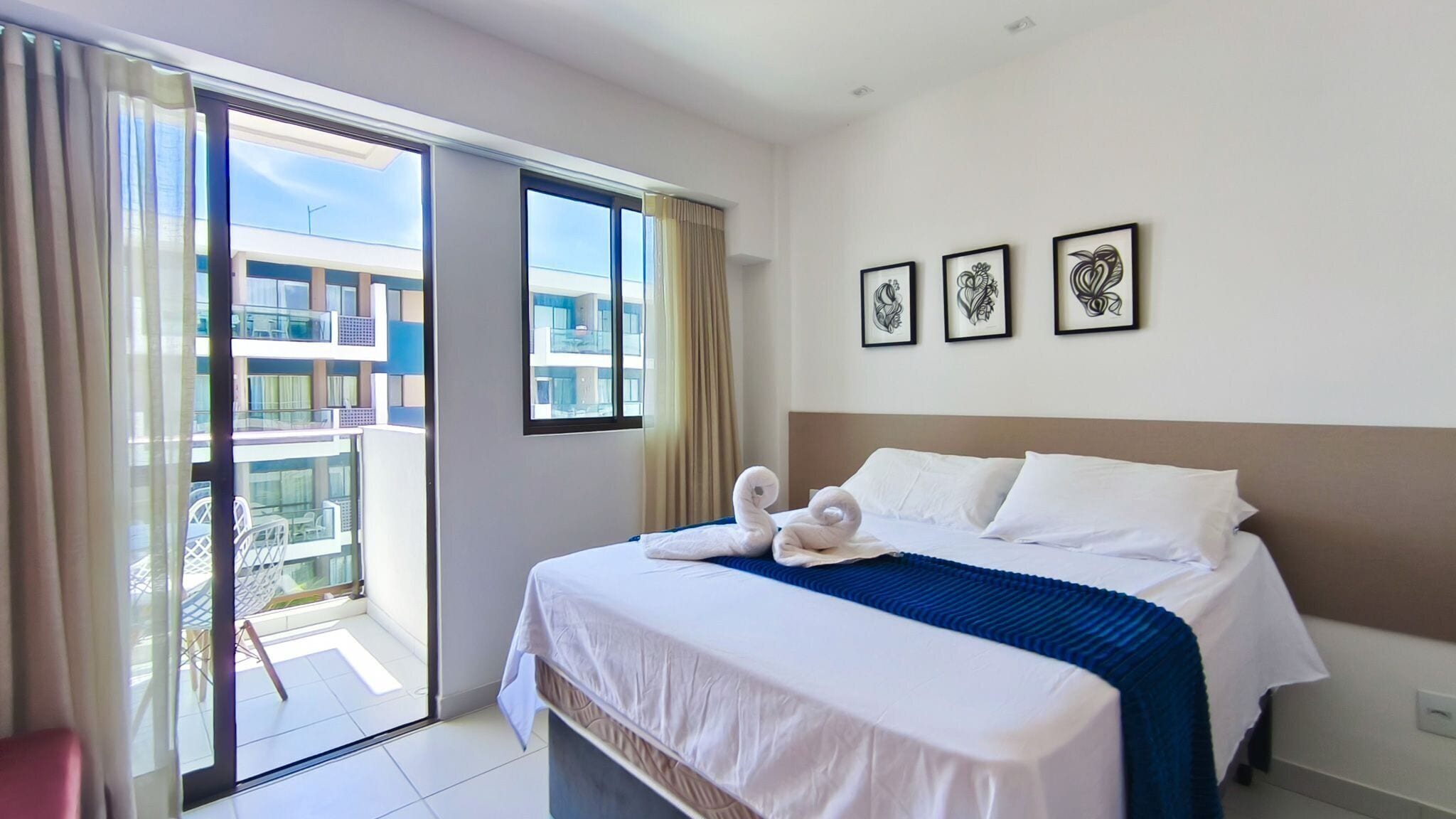 A hotel room with a bed, a balcony, and three framed artworks on the wall.