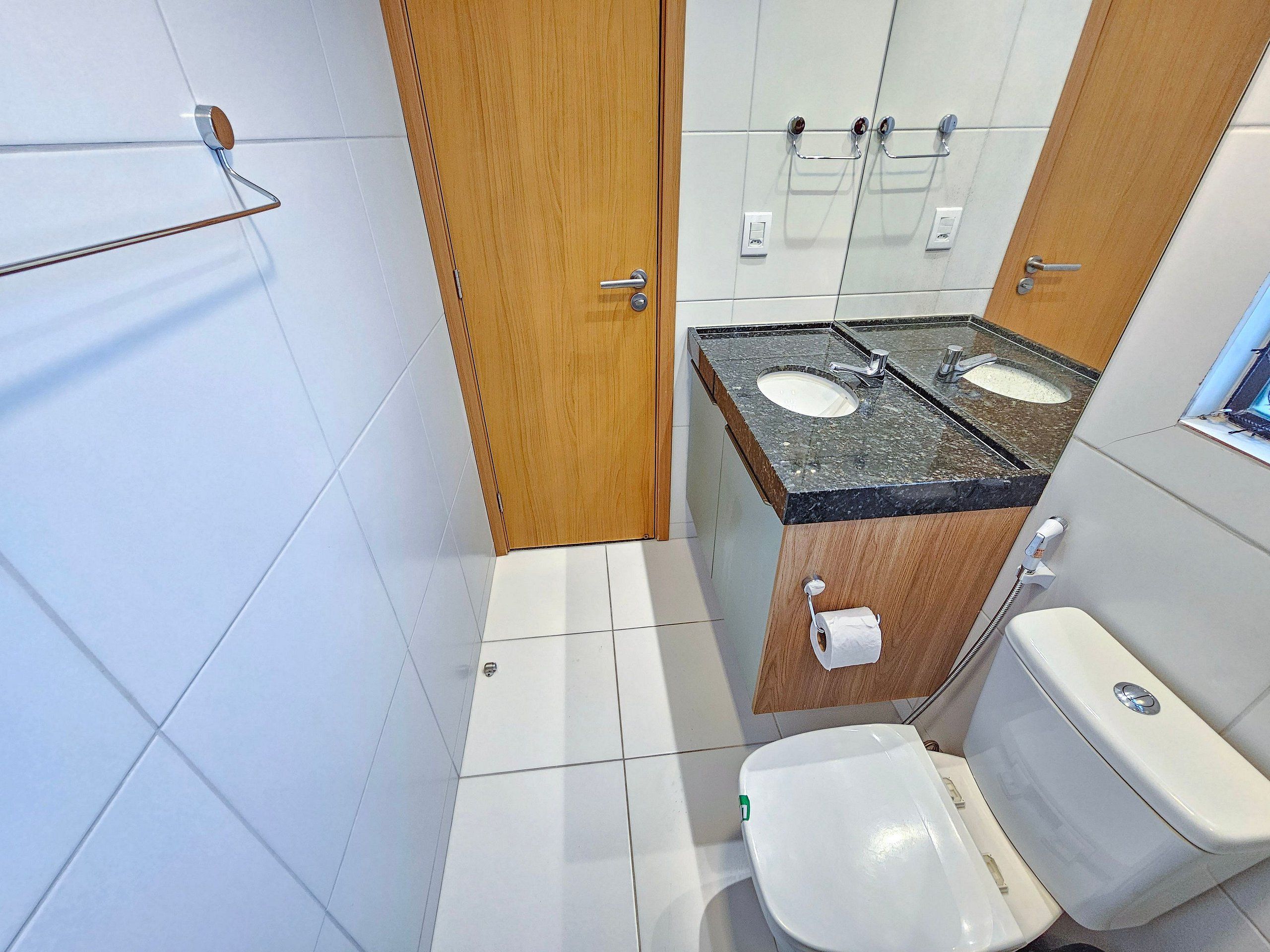 A bathroom with a toilet, two sinks, a shower, and a towel rack.