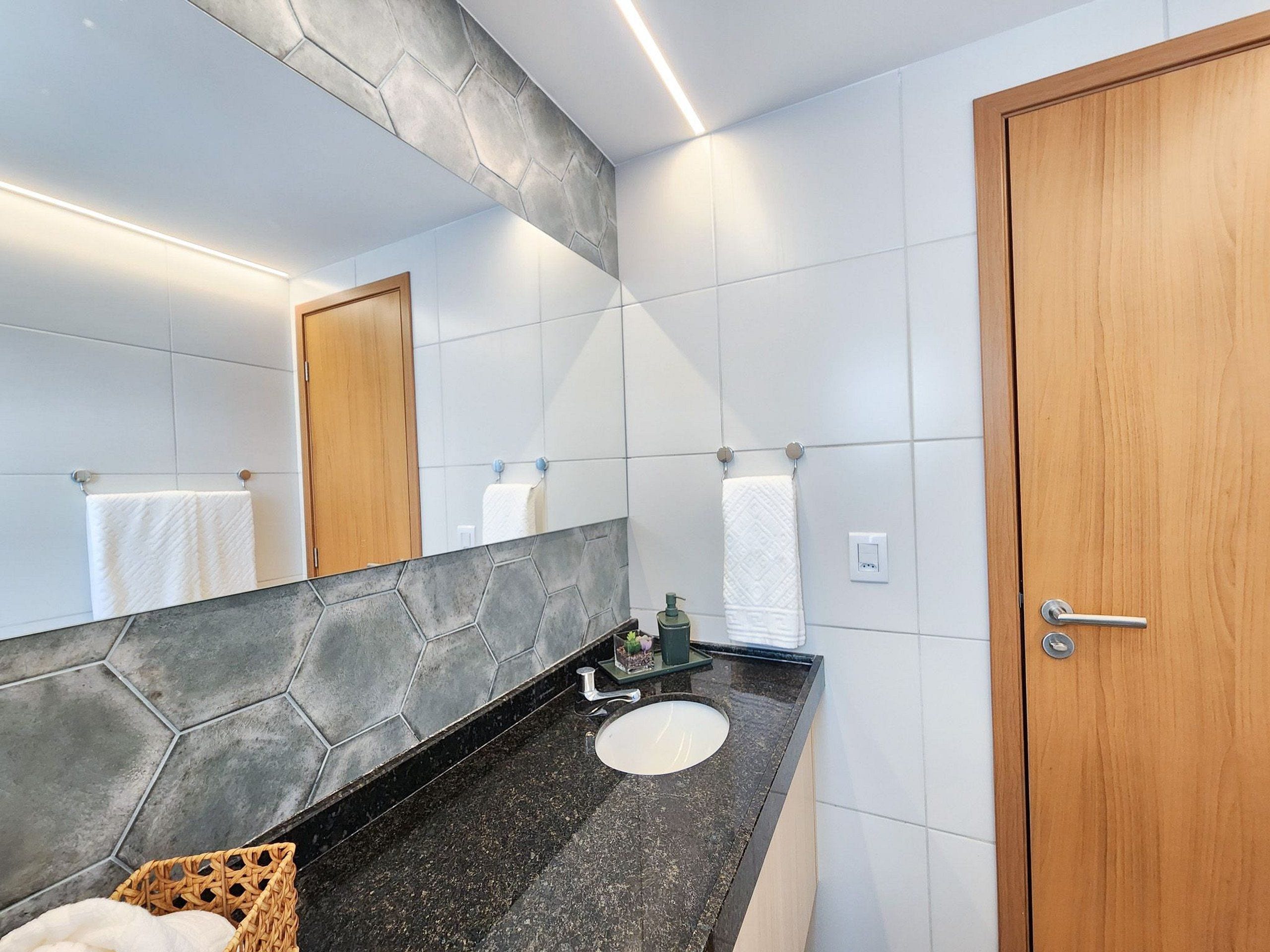 Un baño con encimera de granito, un lavabo redondo, una puerta de madera y un espejo con un salpicadero hexagonal.
