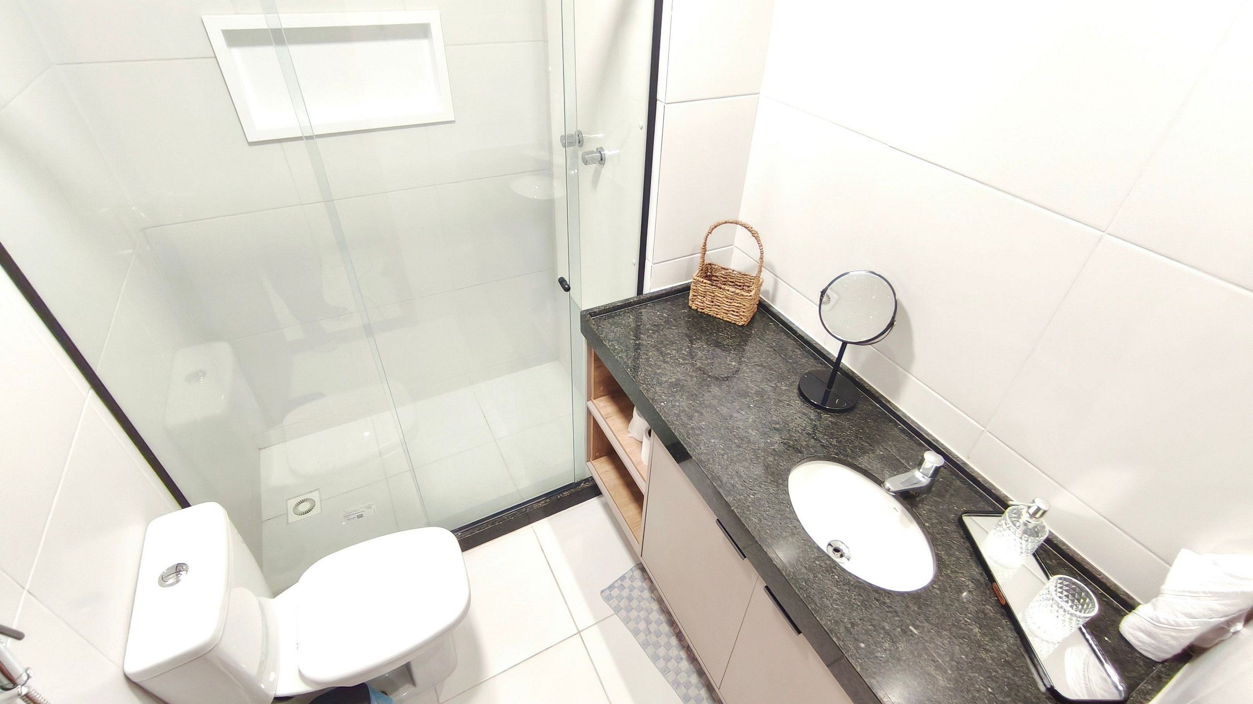 Et badeværelse med bruseniche i glas, en vask med spejl og et toilet.