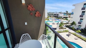 A balcony with a view of a pool area, a white chair, and a table.