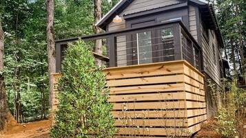 A cabin with a wooden deck and a stone foundation, surrounded by trees.