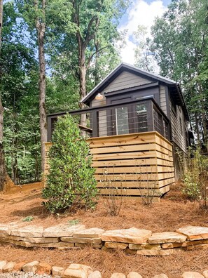 A cabin with a wooden deck and a stone foundation, surrounded by trees.