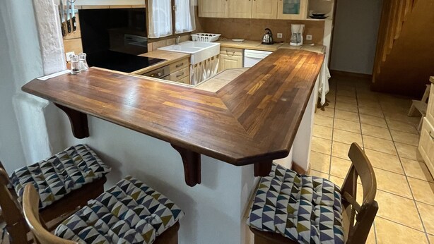 A kitchen with a central island, wooden chairs, and a built-in stove.