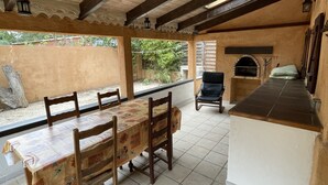 An outdoor patio with a wooden table and chairs, a pizza oven, and a tiled floor.