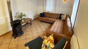 A cozy living room with a brown sofa, a wooden chair, a small table, and a black stove.