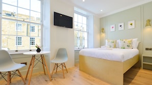 A modern bedroom with a bed, two chairs, a small table, and a TV. - Star Street Serviced Apartments by Concept Apartments (London)