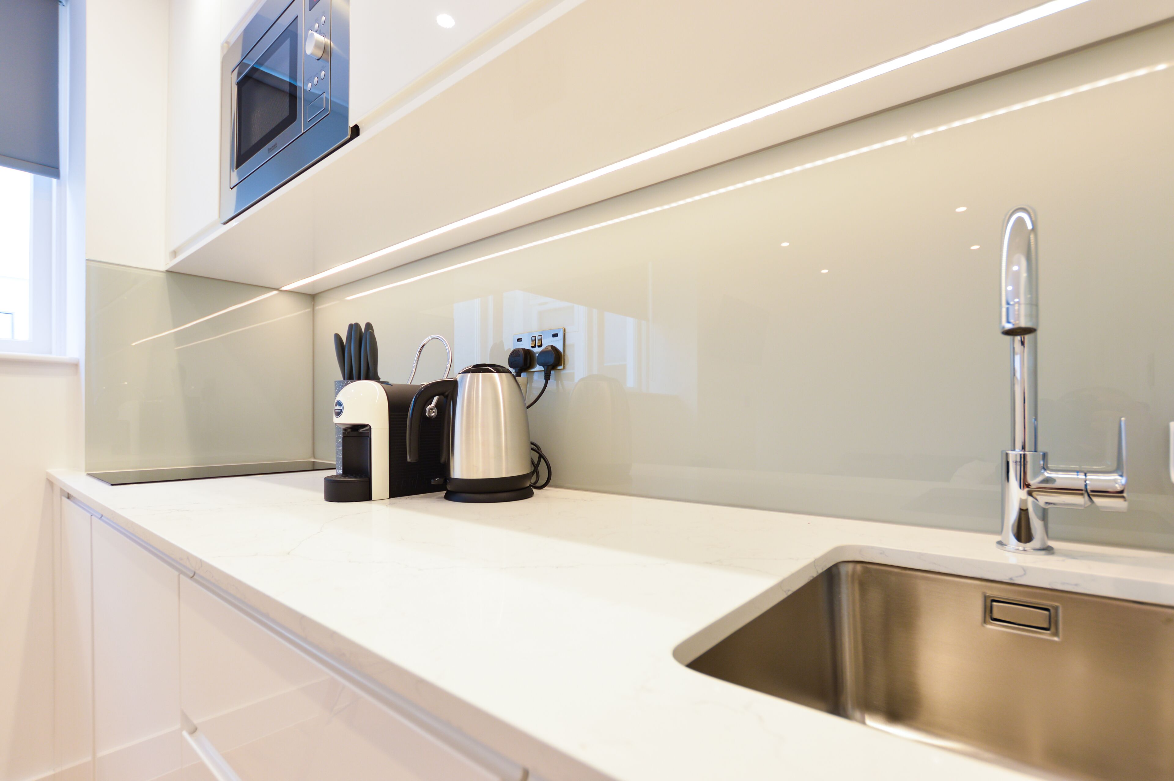 A modern kitchen with a stainless steel sink, a kettle, and a coffee maker on the countertop.
