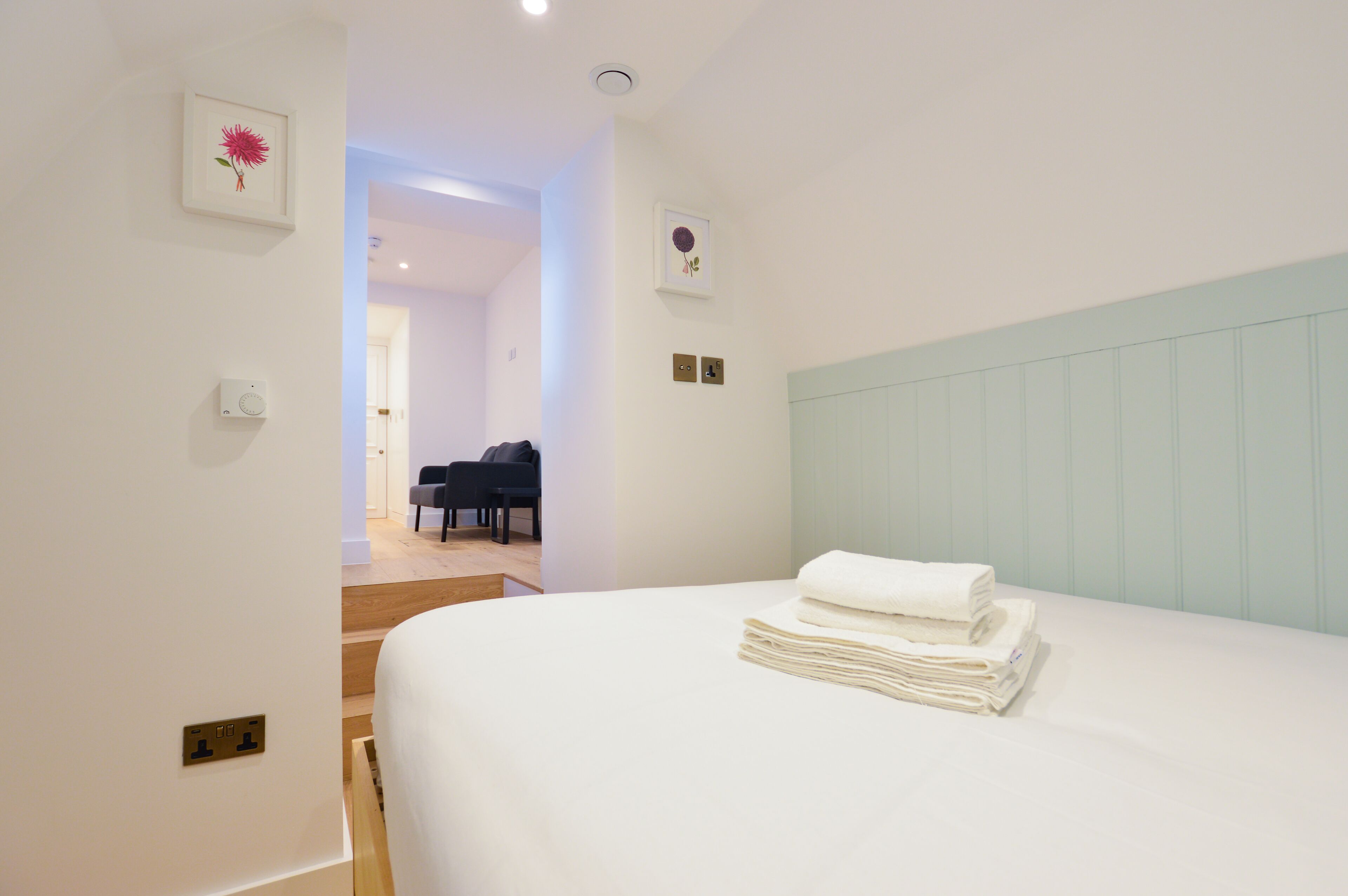A hotel room with a neatly made bed, a chair, and a staircase leading to another room.